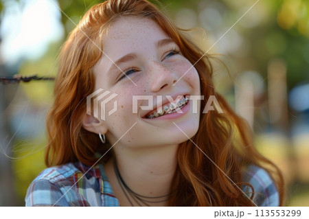 Naturally smiling red-haired teen girl with braces enjoying the sunshine outdoors Naturally smiling red-haired teen girl with braces enjoying the sunshine outdoors 113553299