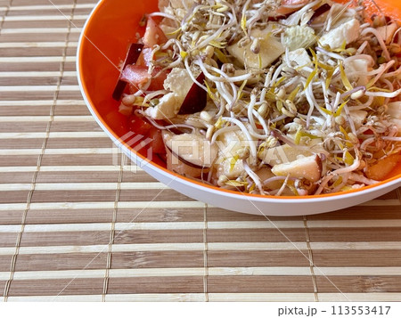 Salad of fresh vegetables and micro-greens. Tomatoes, onions, apples, mound of sprouted mung beans in an orange bowl on bamboo background. Concept of diet, vegan, healthy products. Close up. Salad of fresh vegetables and micro-greens. Tomatoes, onions, apples, mound of sprouted mung beans in an orange bowl on bamboo background. Concept of diet, vegan, healthy products. Close up. 113553417