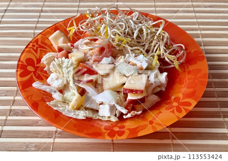 Salad of fresh vegetables and microgreens. Tomatoes, onions, apples, mound of sprouted mung beans in a red plate on bamboo background Salad of fresh vegetables and microgreens. Tomatoes, onions, apples, mound of sprouted mung beans in a red plate on bamboo background 113553424