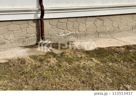 Brown stainless steel drain pipe for drain pipe with water drainage from roof the house to the ground. It attaches to a wall of residential building and leading to concrete surface Brown stainless steel drain pipe for drain pipe with water drainage from roof the house to the ground. It attaches to a wall of residential building and leading to concrete surface 113553437