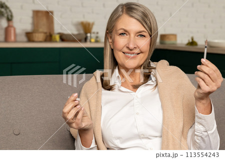 Good-looking diabetic woman with insulin syringe sitting on the sofa at home 113554243