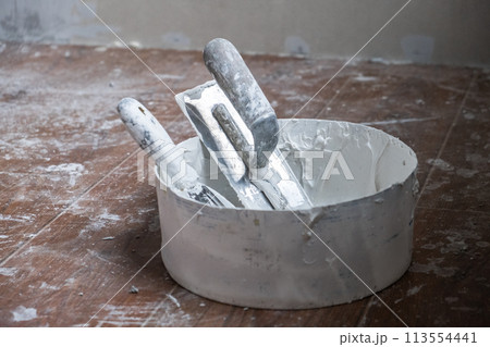 Applying decorative putty. White abstract texture of surface covered with putty. textured background of filler paste applied with putty knife in irregular dashes and strokes. Rough surface plaster 113554441