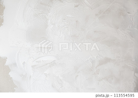 Applying decorative putty. White abstract texture of surface covered with putty. textured background of filler paste applied with putty knife in irregular dashes and strokes. Rough surface plaster Applying decorative putty. White abstract texture of surface covered with putty. textured background of filler paste applied with putty knife in irregular dashes and strokes. Rough surface plaster 113554595