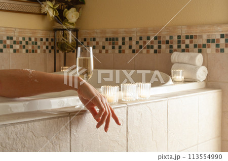 Woman Relaxing in the Bathroom Spa Tub with a Glass of Sparkling Champagne and Candles. 113554990