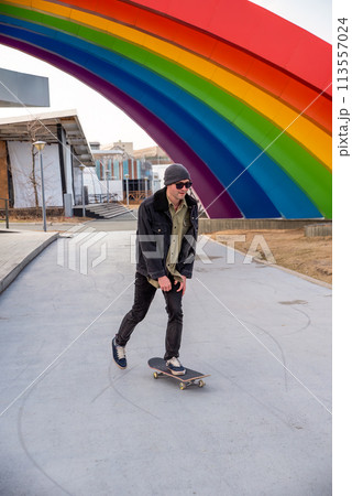 Young man riding a skateboard against composition with rainbow, concept of lgbt style 113557024