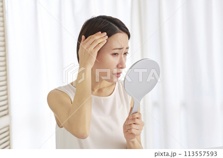 鏡で髪の毛を見て悩む40代の女性 鏡で髪の毛を見て悩む40代の女性 113557593