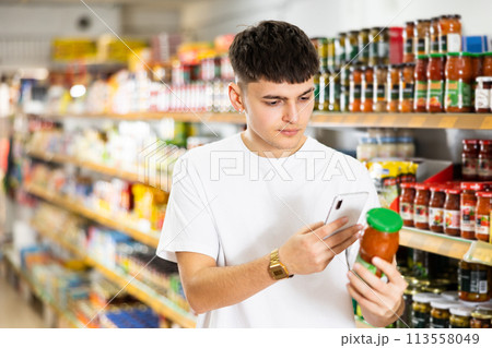 Guy scanning barcode on jar of canned food with phone in supermarket Guy scanning barcode on jar of canned food with phone in supermarket 113558049