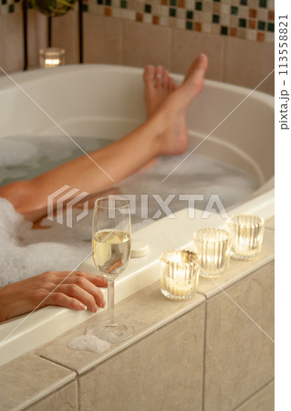 Woman Relaxing in the Bathroom Spa Tub with a Glass of Sparkling Champagne and Candles. 113558821