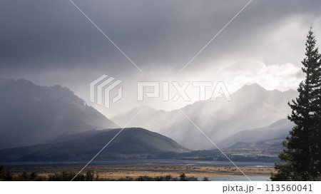 Storm with dark thick clouds raging above alpine landscape with mountain ranges, New Zealand 113560041