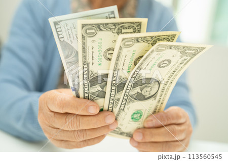 Asian senior woman holding and counting US dollar banknotes money in purse. Poverty, saving problem in retirement. Asian senior woman holding and counting US dollar banknotes money in purse. Poverty, saving problem in retirement. 113560545
