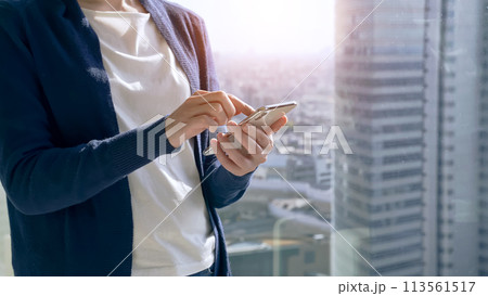 都市を背景にスマホを操作する女性　 113561517