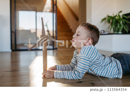 Boy blowing into blades of wind turbine model. Concpet of renewable energy sustainable lifestyle for next generations. 113564354