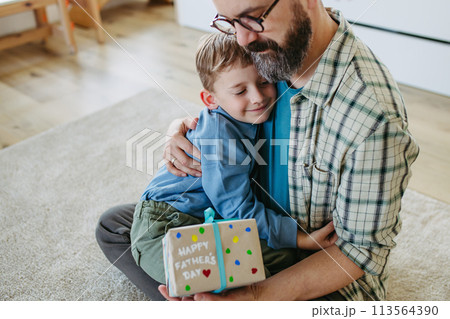 Dad get a handmade gift from little son, present wrapped in diy homemade wrapping paper. Father embracing boy. Happy Fathers day concept. Dad get a handmade gift from little son, present wrapped in diy homemade wrapping paper. Father embracing boy. Happy Fathers day concept. 113564390