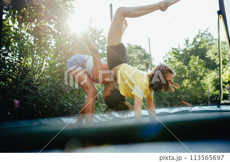 Teenage girls friends outdoors in garden, doing exercise on trampoline, having fun, jumping. 113565697
