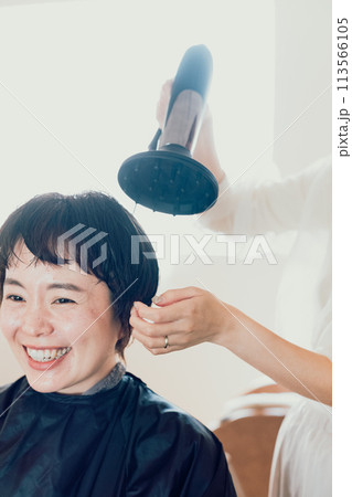 美容院でドライヤーで髪を乾かしてもらう若い女性 113566105