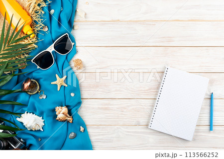 Vacation planning background of notebook seashells, starfish, sunglasses, compass, camera and straw hat on blue fabric and white planks flat lay with copy-space 113566252
