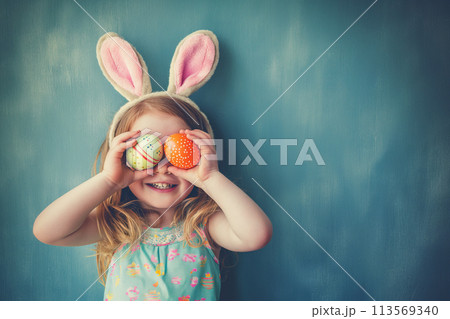 cute little girl with bunny ears holds Easter eggs by the eyes, Easter holiday card with copy space cute little girl with bunny ears holds Easter eggs by the eyes, Easter holiday card with copy space 113569340
