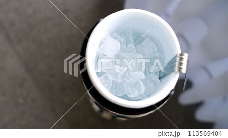 Ice in a blue transparent plastic bucket with ice cube tongs on a table background, top view. Blue ice for champagne in a bucket. 113569404