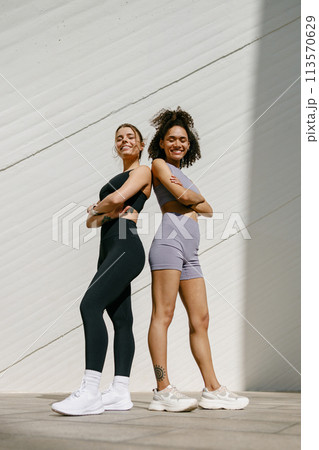 Two young female sportswomen have a rest after morning jogging standing outdoors and looks camera 113570629