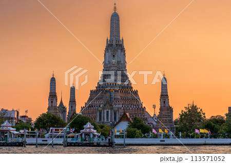 Wat Arun stupa, a significant landmark of Bangkok, Thailand, stands prominently along the Chao Phraya River, with a beautiful sunset sky. 113571052