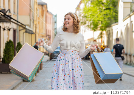 Happy young woman shopaholic consumer after shopping sale with full bags walking in city town street 113571794