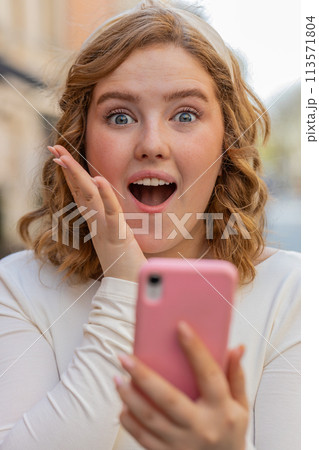 Excited happy winner young woman use smartphone celebrating win good message news in city street 113571804