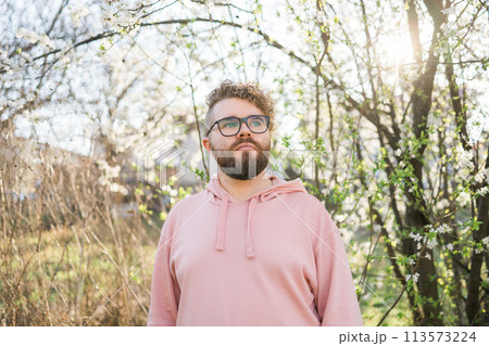 Man with beard and mustache on smiling face near sakura flowers or blooming spring tree. Soft and gentle concept. Bearded man with stylish haircut with flowers on background, close up. Hipster near 113573224
