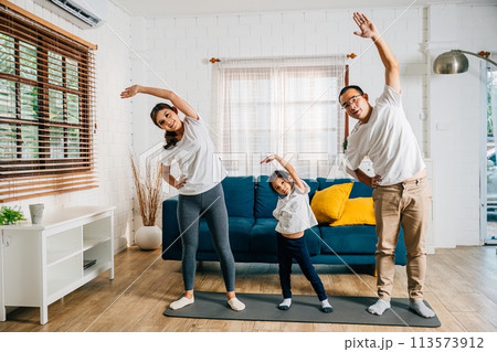 In their domestic setting Asian parents and their daughter enjoy a harmonious family weekend while practicing yoga and fitness training promoting health and education. In their domestic setting Asian parents and their daughter enjoy a harmonious family weekend while practicing yoga and fitness training promoting health and education. 113573912