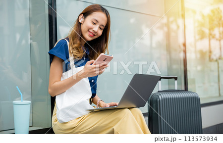 A female entrepreneur works remotely from a train station, her laptop and luggage beside her. She's always on the move, building her business from anywhere. future of work-life balance. A female entrepreneur works remotely from a train station, her laptop and luggage beside her. She's always on the move, building her business from anywhere. future of work-life balance. 113573934