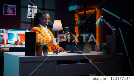 Young woman waving at phone videocall with tutor and classmates, asking for guidance in creating presentations and slideshows. African american student attending online class conference. Camera B. 113577144