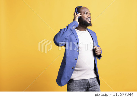 African american man having fun listening to music on headset, dancing around, enjoying songs on radio. BIPOC person feeling relaxed and carefree, hearing tunes, studio background African american man having fun listening to music on headset, dancing around, enjoying songs on radio. BIPOC person feeling relaxed and carefree, hearing tunes, studio background 113577344