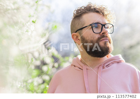 Cool handsome millennial man side face looking away portrait in blooming springtime trees. Blur sakura blossom spring tree background. Copy space 113577402