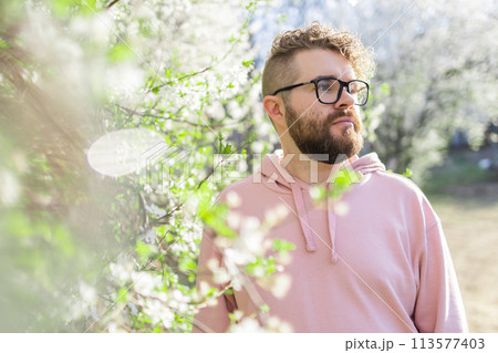 Cool handsome millennial man side face looking away portrait in blooming springtime trees. Blur sakura blossom spring tree background. Copy space 113577403