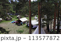 A tent camp with wigwams and bungalows, surrounded by pine trees in the forest. A SUP (stand-up paddleboard) is available for guests to enjoy the calm waters of the lake. Aerial footage. 4k 113577872