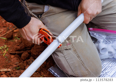 Technician plumber uses special scissors to cut plastic PVC pipe during repair work 113578283