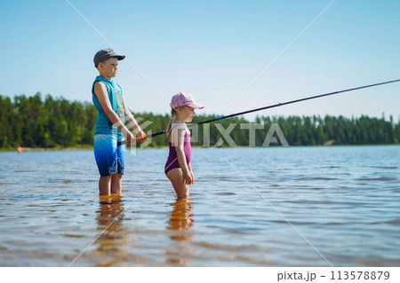 kids fishing standing in the lake. Boy holding a long fish rod kids fishing standing in the lake. Boy holding a long fish rod 113578879