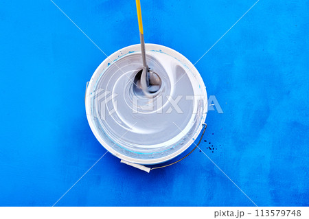 Tinting and mixing paint with stirring rod or mixer for paints, house painter added toner pigment to bucket, blue background. 113579748