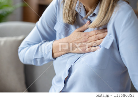 Close-up image of a senior woman experiencing discomfort and holding her chest, possibly indicating heart problems or a heart attack. Close-up image of a senior woman experiencing discomfort and holding her chest, possibly indicating heart problems or a heart attack. 113580353