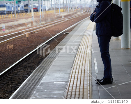 冬の駅で電車待ちの若い男性サラリーマンの姿 冬の駅で電車待ちの若い男性サラリーマンの姿 113581140