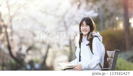 The concept of a college student sitting on a bench in a school park, reading a book and studying, and a high school student smiling brightly while carrying a bag. 113581427