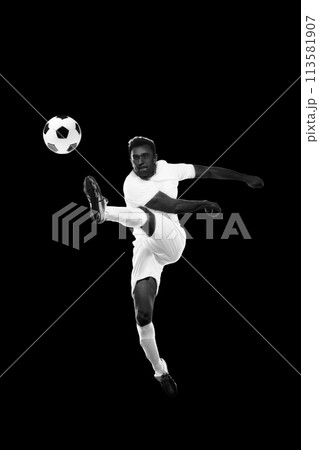 Monochrome dynamic image of young man, soccer player in motion hitting ball in a jump on black background 113581907
