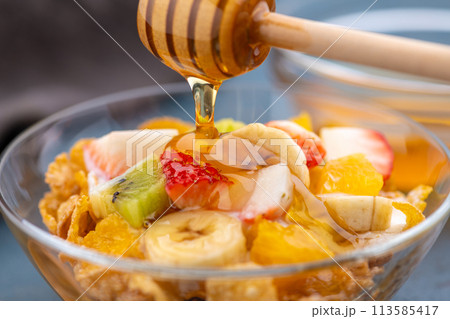 フルーツをのせた朝食ヨーグルトシリアルにハチミツをかける フルーツをのせた朝食ヨーグルトシリアルにハチミツをかける 113585417