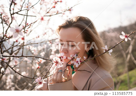 A woman is smelling a flower in a field. Concept of peace and tranquility, as the woman is surrounded by nature and taking a moment to appreciate the beauty of the flower. 113585775