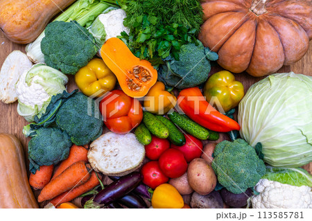 Various vegetables are laid out on a wooden table. Large assortment of vegetables food. pumpkin cabbage broccoli pepper tomatoes carrots and others 113585781