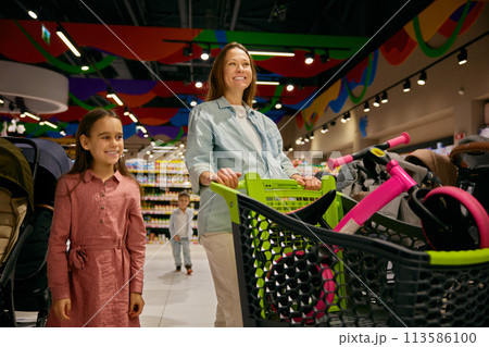 Positive pregnant mother and daughter doing purchases at toys store department 113586100