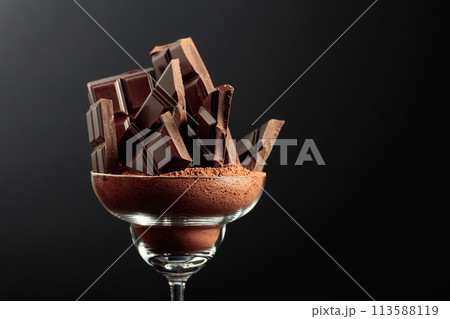 Broken black chocolate bar in glass with cocoa powder. 113588119