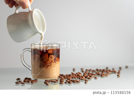 Pouring milk in black coffee. 113588156