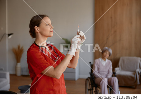 Woman nurse preparing syringe for vaccination of old lady patient 113588204