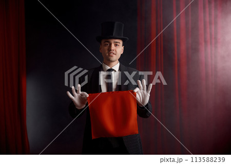Young male magician actor showing trick with napkin in mysterious atmosphere 113588239