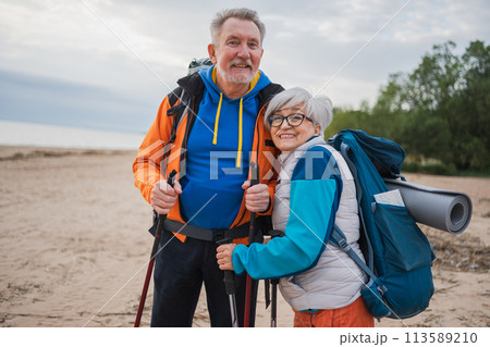 Hiking tourism adventure. Senior couple man woman enjoying outdoor recreation hiking on beach. Happy old people backpackers hikers enjoy walking hike trekking tourism active vacation beauty of nature Hiking tourism adventure. Senior couple man woman enjoying outdoor recreation hiking on beach. Happy old people backpackers hikers enjoy walking hike trekking tourism active vacation beauty of nature 113589210